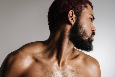 Siyah tişörtsüz sakallı adam beyaz arka planda yalnız poz veriyor ve yan tarafa bakıyor.