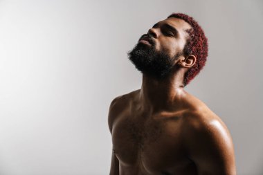 Siyah gömleksiz sporcu kamerada poz veriyor, gözleri kapalı, beyaz arka planda izole halde.