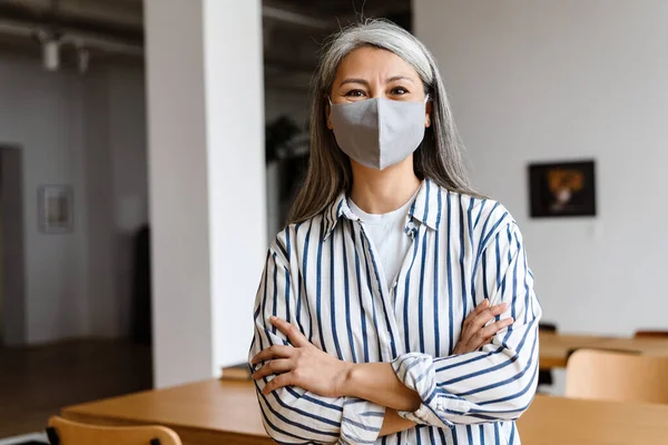 Confident woman office worker in face mask standing arms folded