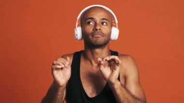 Portakal rengi stüdyoda müzik dinleyen ve dans eden kulaklıklı mutlu bir İspanyol.