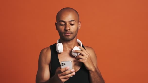 Hombre Hispano Sonriente Con Auriculares Mirando Teléfono Estudio Naranja — Vídeo de stock