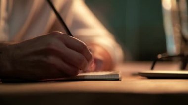 Gece vakti erkek ellerinin not defterine bir şey yazışının yakın görüntüsü.