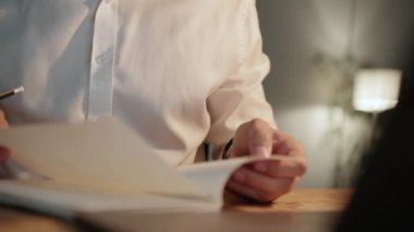 Ofiste akşam saatlerinde erkek ellerinin deftere baktığı yakın çekim görüntüsü.