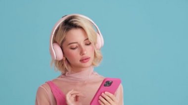 Telefonunda müzik çalan ve mavi stüdyoda dans eden gülümseyen kadının yakın çekim görüntüsü.