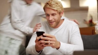 Gülümseyen oğul kanepede babasına atlıyor ve telefondaki kaseti çeviriyor.