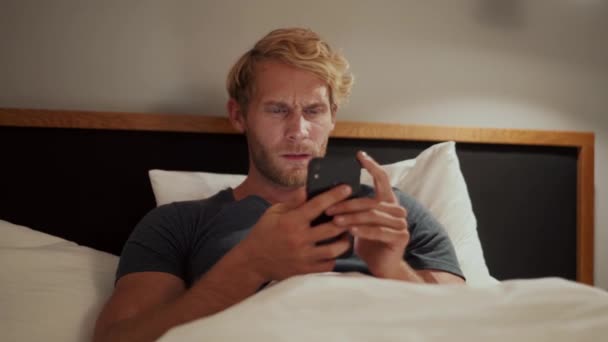 Yatakta Yatarken Telefonda Bant Yapıştıran Gülümseyen Adam — Stok video