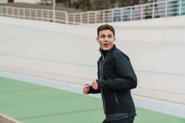 Stadyumda koşup kulaklıkla müzik dinleyen kendine güvenen genç bir adam.