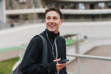 Kulaklıkları ve cep telefonlarıyla stadyumda müzik dinleyen yakışıklı sporcu.