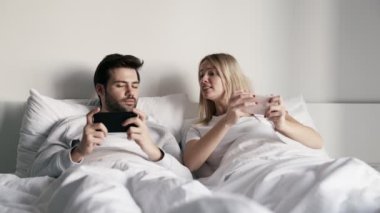 Telefonda oyun oynayan gülümseyen bir çift ve zaferle sevinen bir kız yatakta yatıyor.