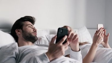 Sabahları konuşan ve ellerinde telefonla yatakta yatan bir çift.