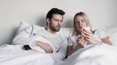 Kendine güvenen bir kadın telefonda erkek arkadaşına bir şey gösteriyor ve yatakta yatarken konuşuyor.