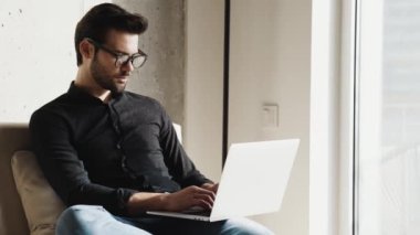 Gözlüklü ciddi bir işadamı evde dizüstü bilgisayarla çalışıyor.