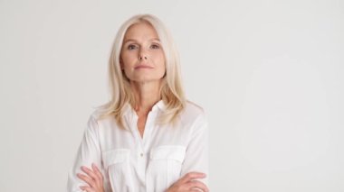 Ciddi bir yetişkin kadın el ele tutuşup beyaz stüdyodaki kameraya bakıyor.