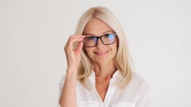 Gülen olgun kadının yakın plan görüntüsü beyaz stüdyoda gözlüğünü çıkarıyor.