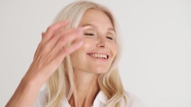 Gülümseyen olgun kadının beyaz stüdyodaki kamerada saç stilini düzeltirken yakın plan görüntüsü.