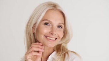 Beyaz stüdyoda kameraya poz veren gülümseyen olgun kadının yakın görüntüsü.