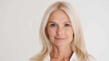 Beyaz stüdyodaki kameraya bakan kendine güvenen olgun kadının yakın görüntüsü.