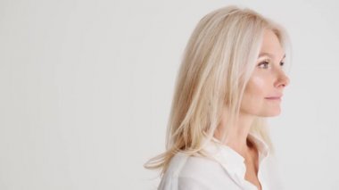 Beyaz stüdyodaki kameraya bakan konsantre olmuş olgun kadının yan görüntüsü.