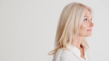 Beyaz stüdyodaki kameraya bakan gülümseyen olgun kadının yan görüntüsü.