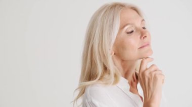 Beyaz stüdyoda ciddi bir yetişkin kadının yüzüne dokunuşunun yan görüntüsü