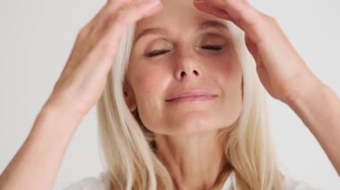 Gülümseyen olgun kadının kamera karşısında saç stilini düzeltirken beyaz stüdyodaki bir ayna gibi yakın plan görüntüsü.