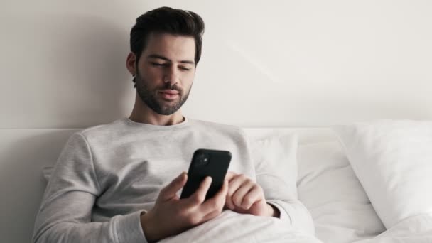 Красивий Чоловік Вимикає Телефон Намагається Спати Лежачи Ліжку — стокове відео