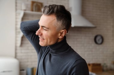 Yakışıklı memnun adam gülümsüyor ve ev mutfağına bakıyor.