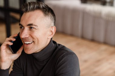 Evde gülümseyen ve telefonla konuşan yakışıklı adam.