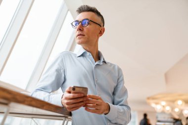 Kapalı bir kafede cep telefonu kullanan kendine güvenen yakışıklı iş adamı.