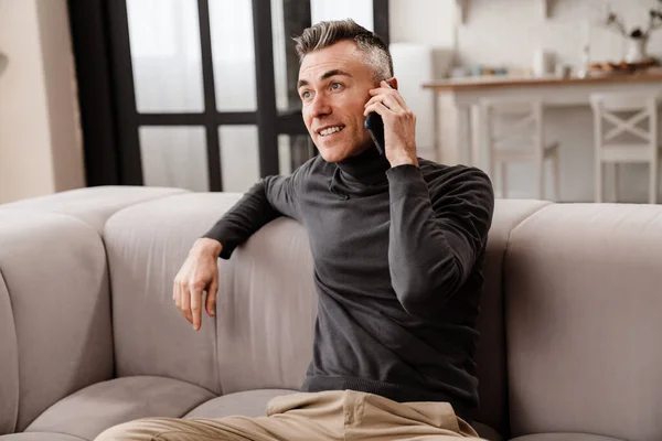 Happy man talking on mobile phone while sitting on a couch at home