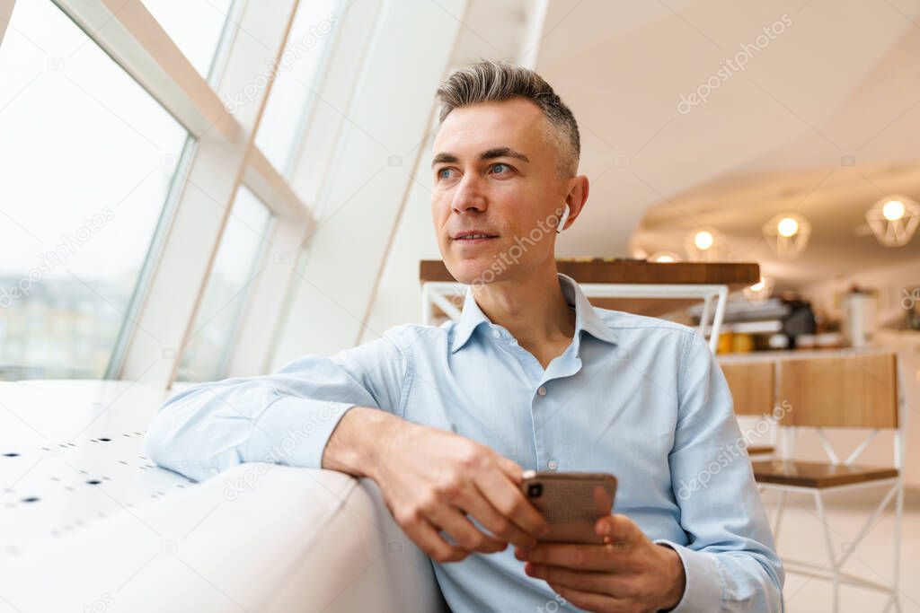 Confident handsome businessman using smartphone in cafe indoors