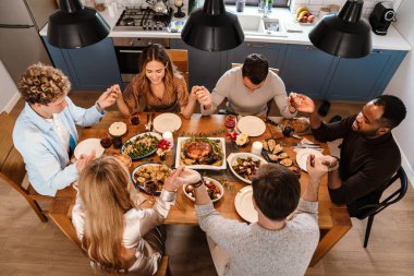 Memleketteki Şükran Günü yemeğinde el ele tutuşup dua eden çok ırklı arkadaşlar.