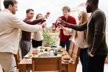 Çok ırklı mutlu arkadaşlar Şükran Günü yemeği sırasında dışarıda şarap içiyorlar.