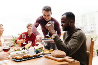 Dışarıda şükran günü yemeği yerken gülen ve konuşan çok ırklı mutlu arkadaşlar.