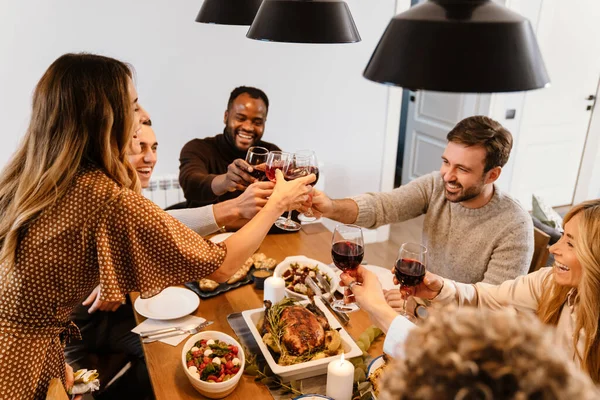 Multiracial happy friends drinking wine during thanksgiving dinner at home