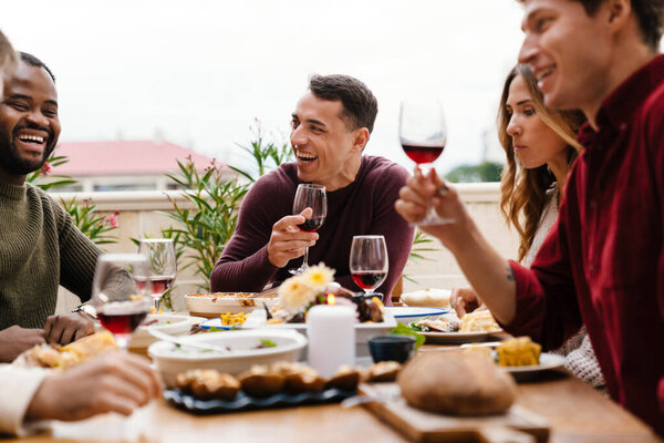 Multiracial happy friends laughing and talking during thanksgiving dinner outdoors