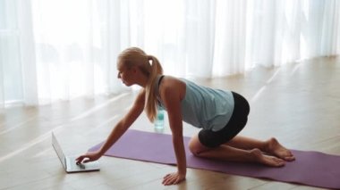Yakışıklı kadın dizüstü bilgisayarla eğitime başlıyor ve evde yoga egzersizi yapıyor.