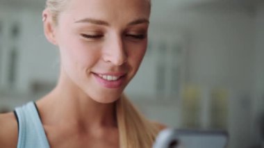 Gülümseyen sarışının yakından görüntüsü. Telefonla mesaj atan ve evine bakan sarışın kadın.