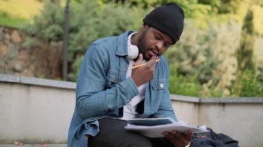 Kulaklıklı dalgın bir Afrikalı kafasını sallıyor ve beton bir bankta not defterine bir şeyler yazıyor.