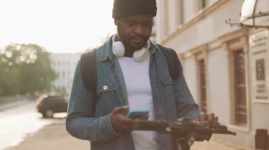 Kulaklıklı Afrikalı adam sokaktaki bir scooterın QR kodunu tarıyor.