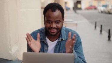 Dışarıdaki kafede dizüstü bilgisayarla konuşan pozitif Afrikalı adam.