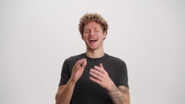 Gülen kıvırcık saçlı tişörtlü adam beyaz stüdyoda kameraya bakıyor.