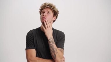 Beyaz stüdyoda bir şeyler düşünen dalgın bir adam.