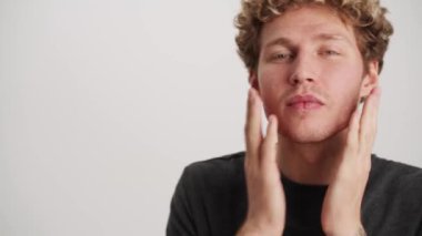 Kıvırcık saçlı adam beyaz stüdyodaki görüntüsünü düzeltiyor.