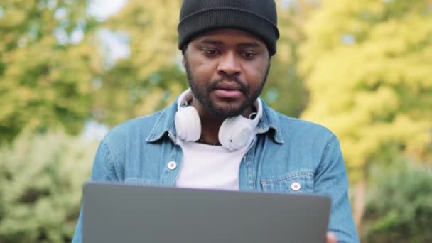 Skoncentrowany Afrykanin Słuchawkach Czyta Coś Laptopie Parku — Wideo stockowe