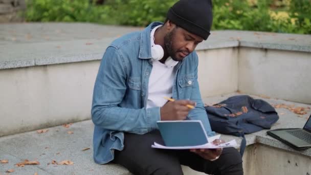 Pensive African Man Headphones Writing Something Notepad Concrete Bench — Stock video