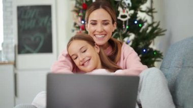 Gülümseyen anne ve kız dizüstü bilgisayardan komik bir şey izliyorlar.