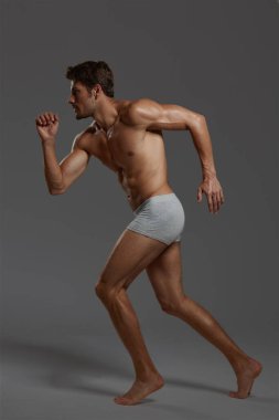 Genç, konsantre Avrupalı atletik adamın profili. Çıplak spor gövdeli, iç çamaşırlı sakallı bir adam. Koyu gri arka planda izole edilmiş. Stüdyo çekimi. Boşluğu kopyala
