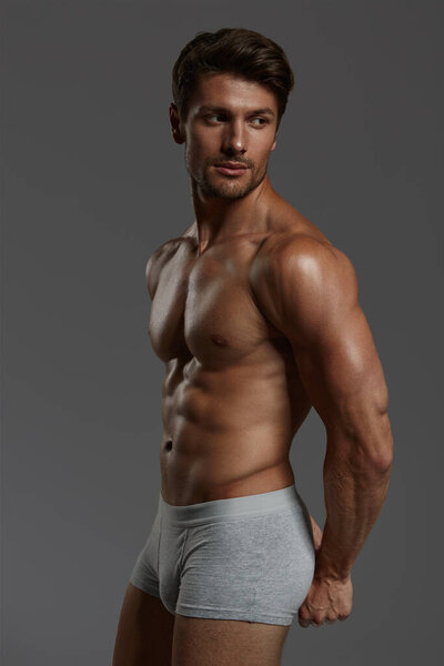 Молодой красивый сфокусированный европейский спортсмен. Боковой вид бородатого мужчины с темными волосами и голым спортивным туловищем. Изолирован на темно-сером фоне. Студийные съемки
