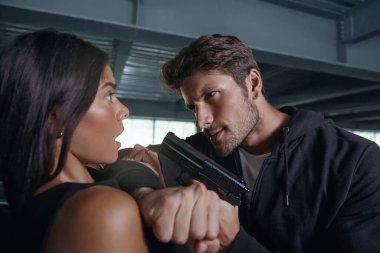 Saldırgan soyguncu korkmuş kızı silahla tehdit ediyor. Avrupalı genç esmer kadın. Erkek haydutlar siyah kapüşonlu giyer. Soygun ve adam kaçırma kavramı